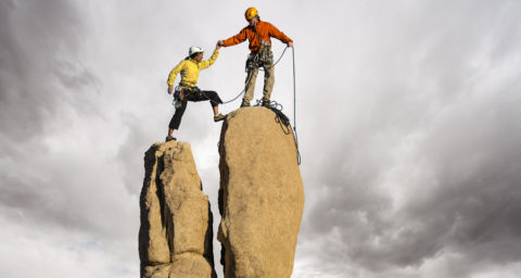 man and woman climbing to top of rock