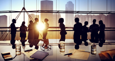 Silhouette of businessmen and women in conference room with setting sun and skyline background
