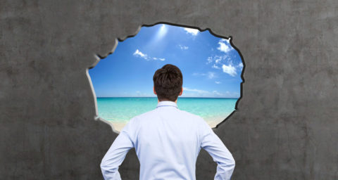 business man looking through hole in wall at a beach