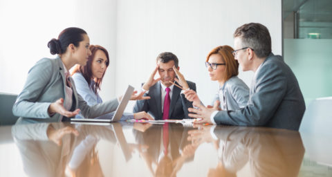 business man holding head as others around him argue in meeting