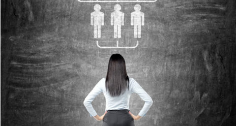 business woman standing in front of a chalkboard illustration of delegating
